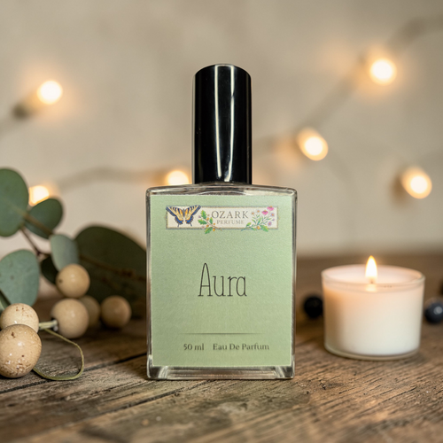 Perfume bottle labeled 'Aura' by Ozark Aromatics on a wooden surface with decorative elements.