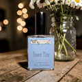 Perfume bottle labeled 'Power Play' by Ozark Perfume on a wooden surface with flowers in the background.