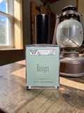 Perfume bottle labeled 'Reign' by Ozark on a wooden surface with a lantern in the background.