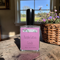 Perfume bottle labeled 'Purple Cotton Candy' by Ozark on a wooden table with a window and flowers in the background.