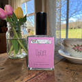 Ozark Perfume bottle labeled 'Uplift' on a wooden table with flowers and a teacup in the background.