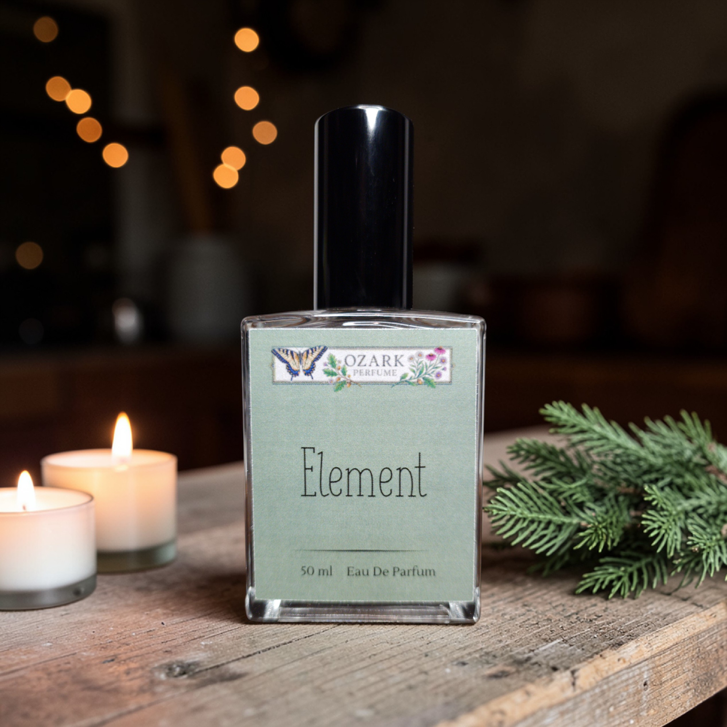 Perfume bottle labeled 'Element' by 'Ozark Perfume' on a wooden surface with candles and greenery.