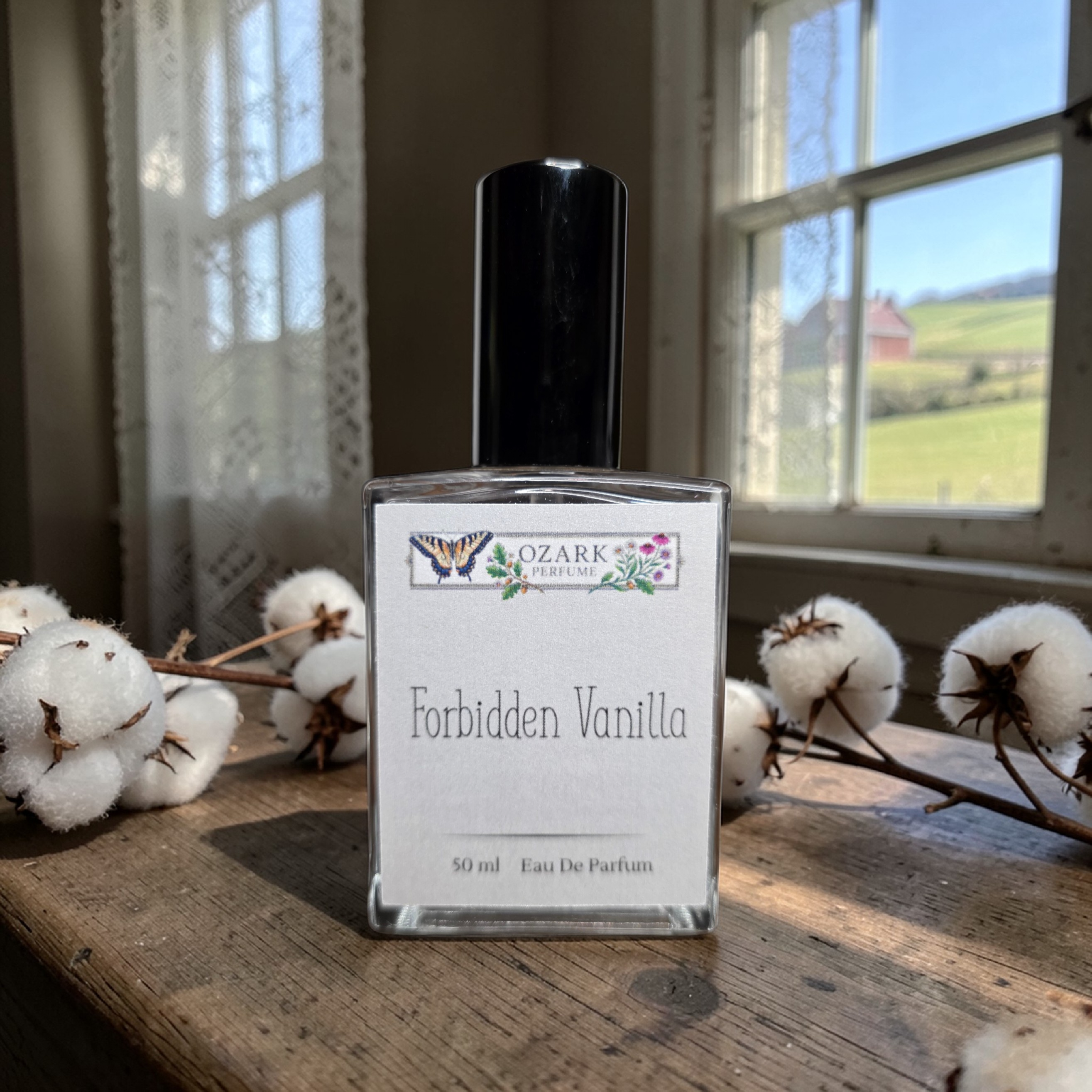 Perfume bottle labeled 'Forbidden Vanilla' by Ozark Aromatics on a wooden surface with cotton branches.