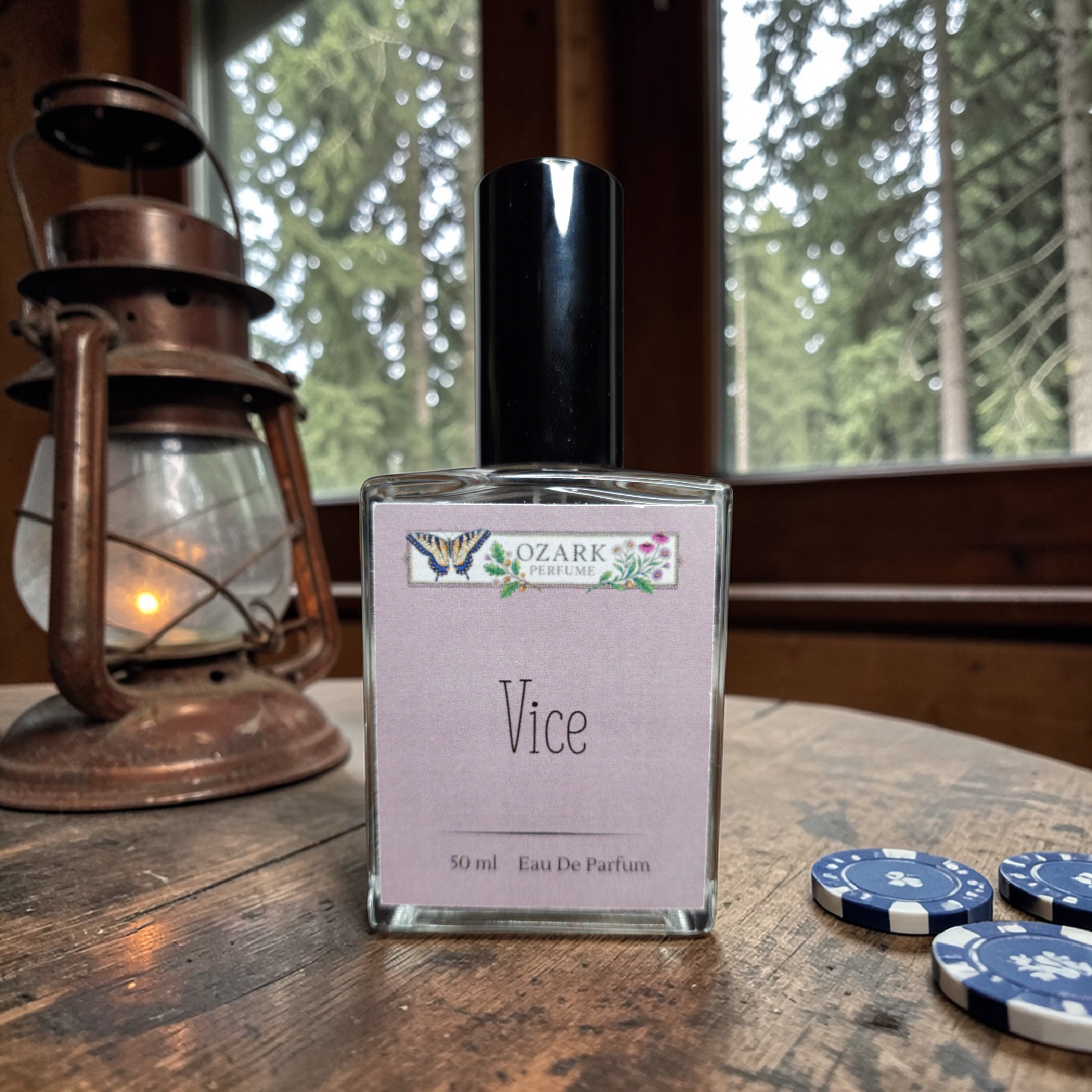 Perfume bottle labeled 'Vice' by Ozark Trading Co on a wooden surface with a lantern and poker chips in the background.