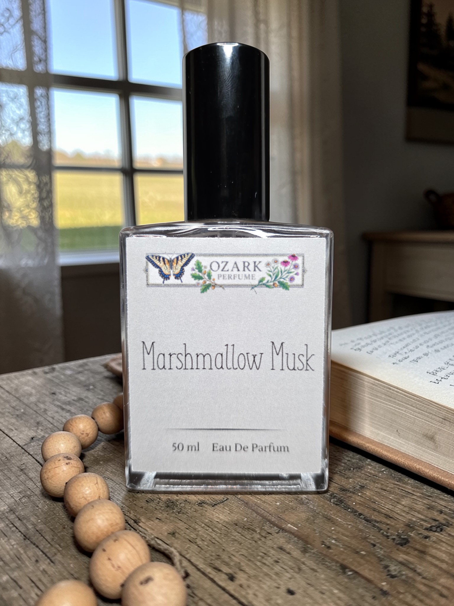 Bottle of 'Marshmallow Musk' perfume by Ozark Perfume on a wooden surface with a window in the background.