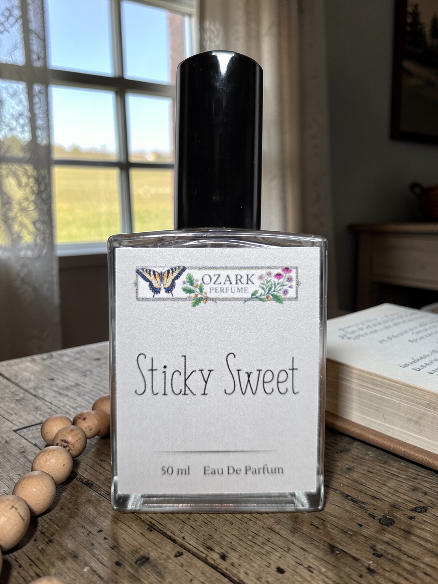 Bottle of 'Sticky Sweet' eau de parfum by Ozark Perfume on a wooden surface with a window in the background.