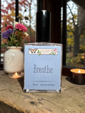 Ozark Essentials 'Breathe' eau de parfum bottle on a wooden surface with candles and flowers in the background.