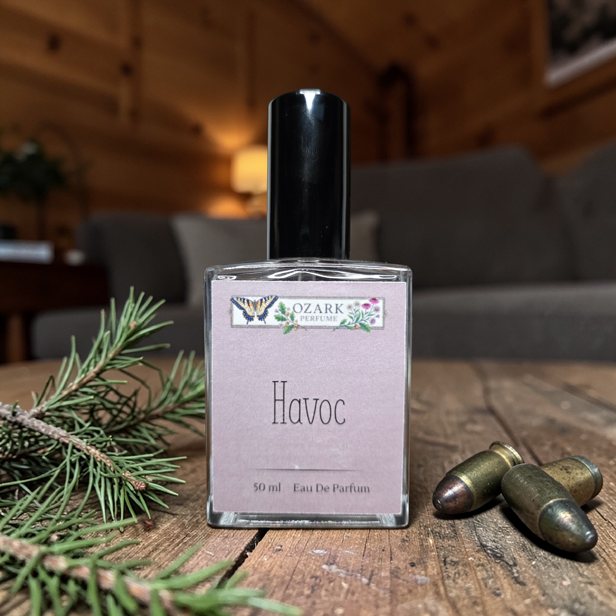 Perfume bottle labeled 'Havoc' by Ozark Perfume Co. on a wooden surface with greenery and bullets.