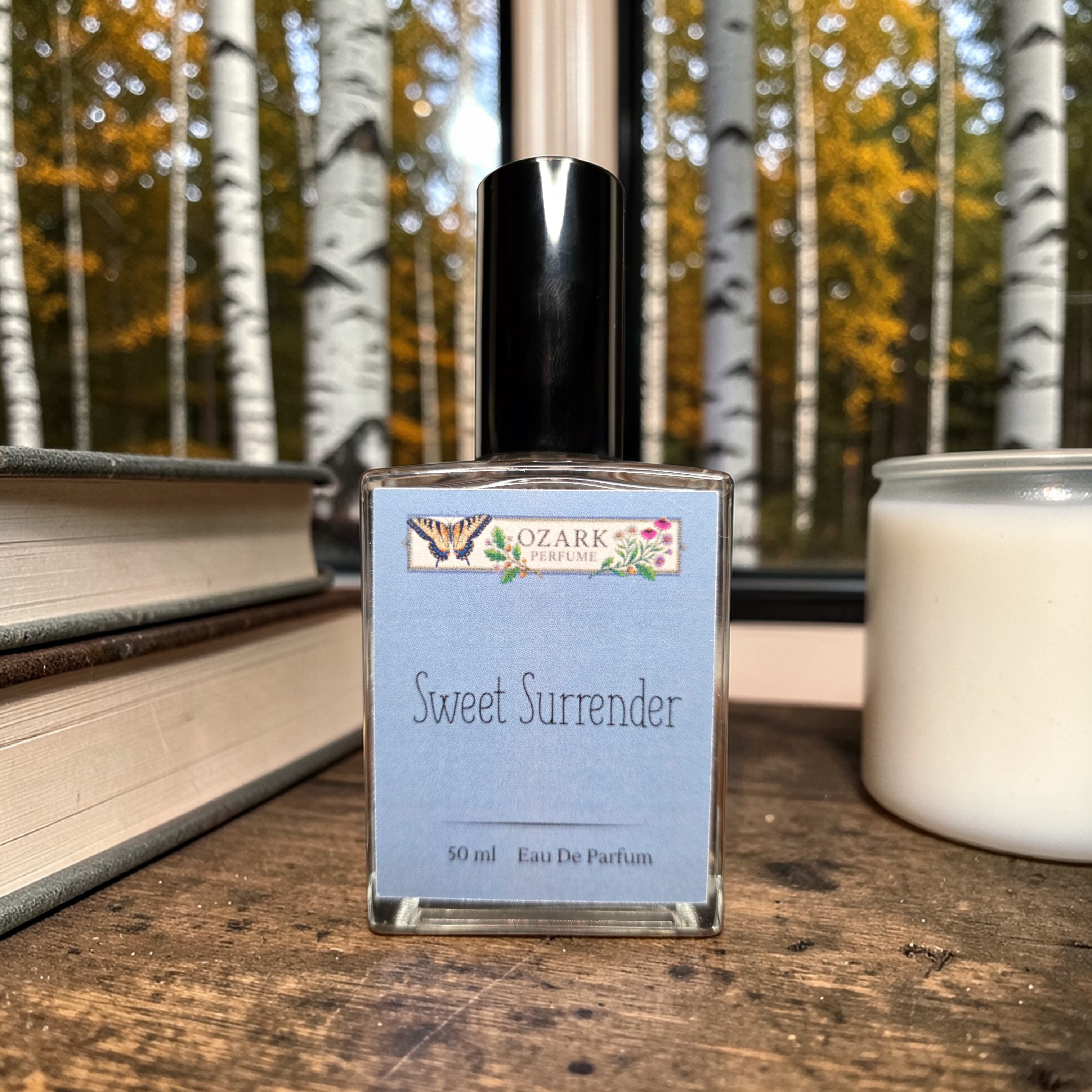 Ozark Perfume bottle labeled 'Sweet Surrender' on a wooden surface with a forest background