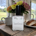 Perfume bottle labeled 'Sweetbread' on a wooden surface with flowers and bread in the background.