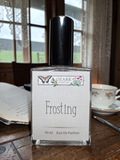 Frosting perfume bottle by Ozark Perfume on a wooden table with a book and tea cup in the background.