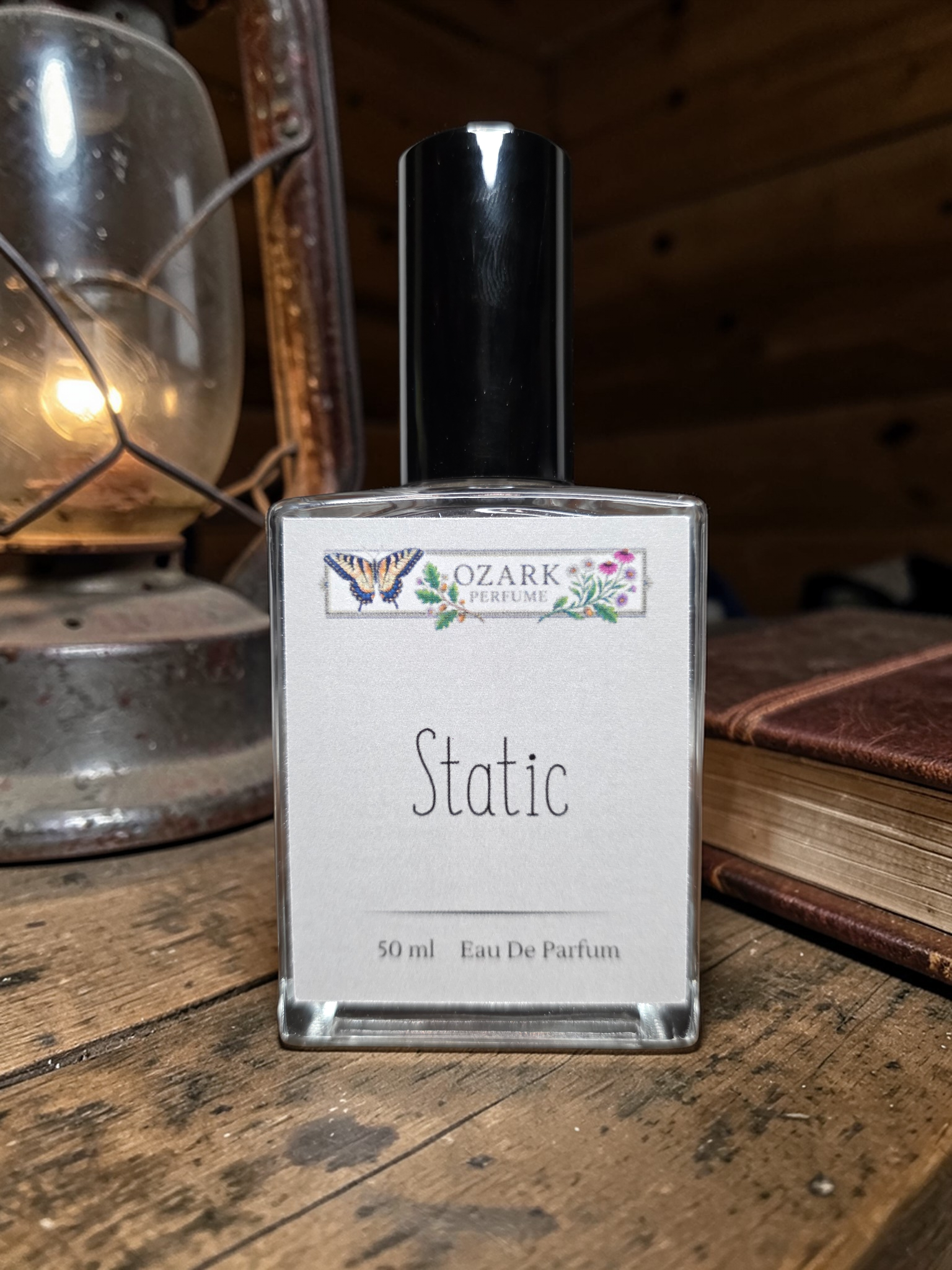 Perfume bottle labeled 'Static' by Ozark Aromatics on a wooden surface with a vintage lantern and book in the background.