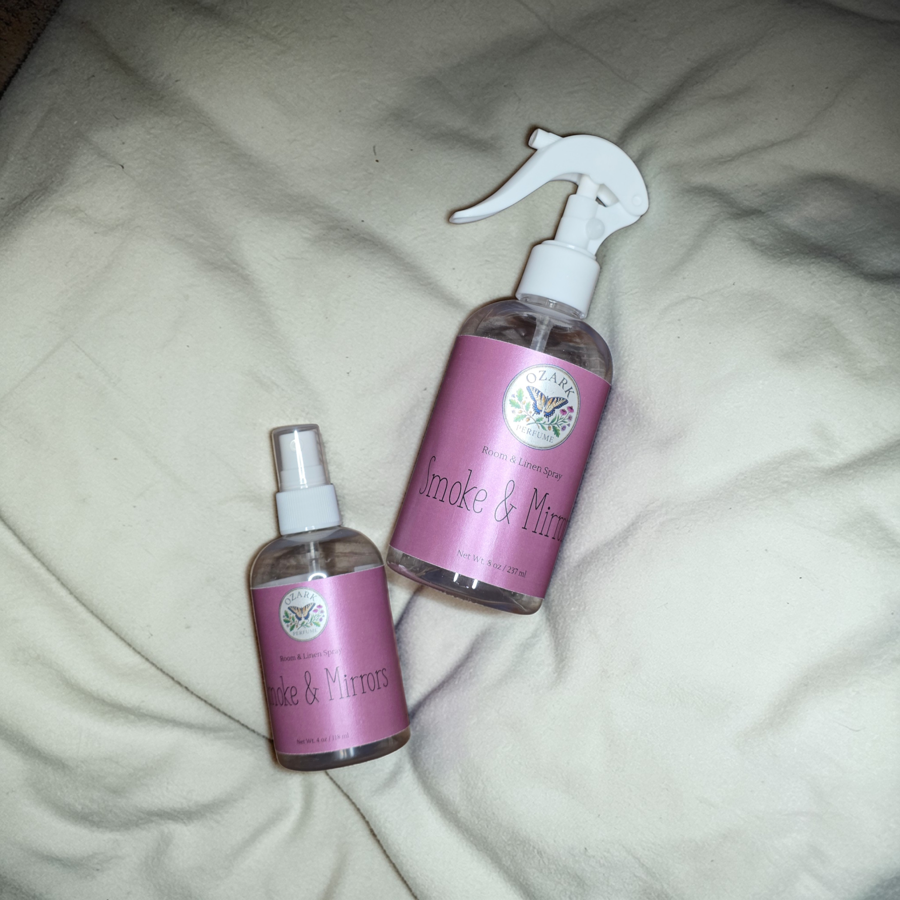Two bottles of 'Smoke & Mirrors' product on a textured surface