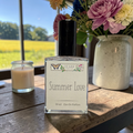 Ozark Perfume bottle labeled 'Summer Love' on a wooden table with a window view of a field.