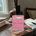 Bottle of Ozark Perfume 'Sugar Zoomies' on a wooden table with books and a vase in the background.