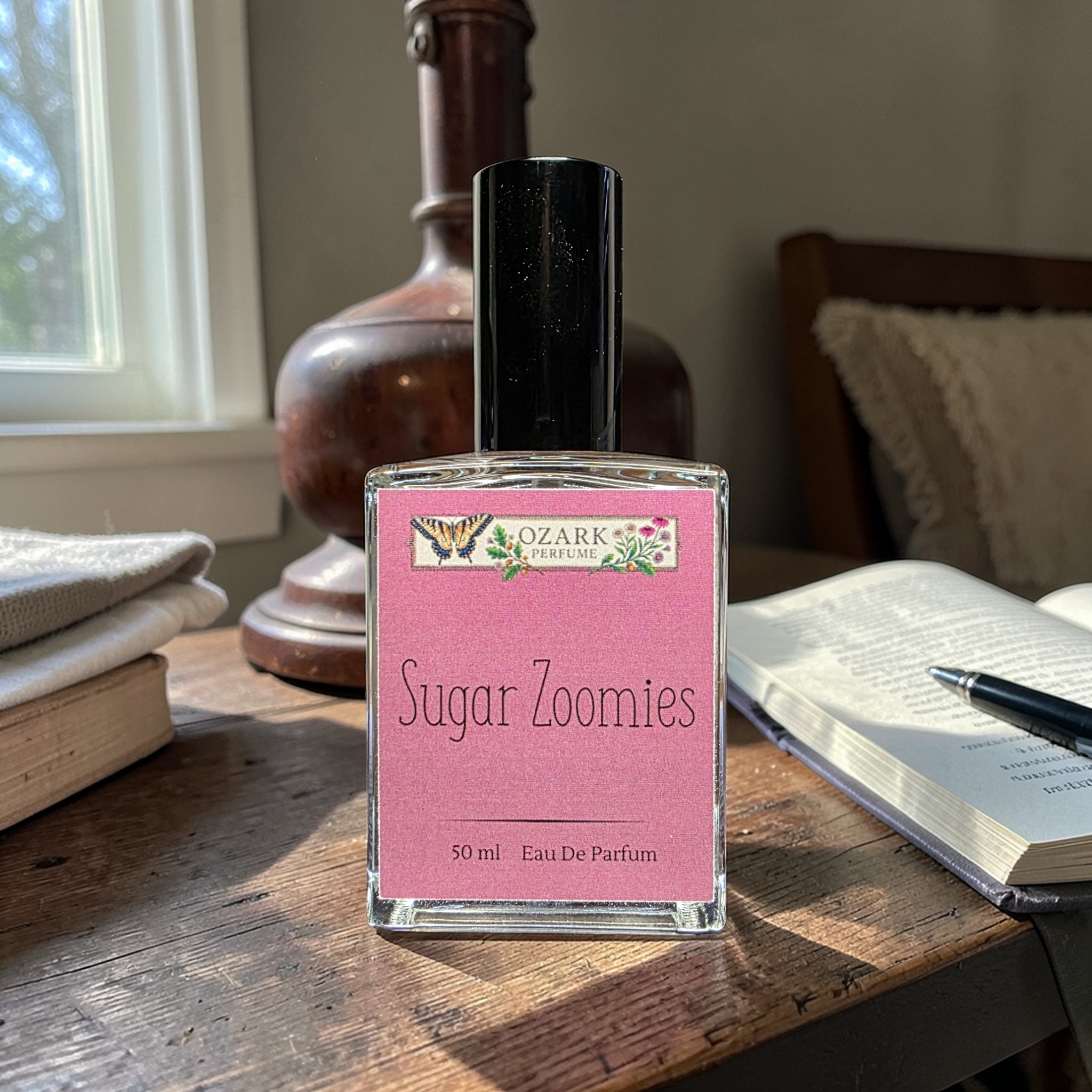 Bottle of Ozark Perfume 'Sugar Zoomies' on a wooden table with books and a vase in the background.