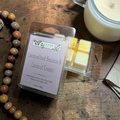 Packaged wax melts with caramelized banana and coconut cream on the label on a wooden surface with a candle and beads.