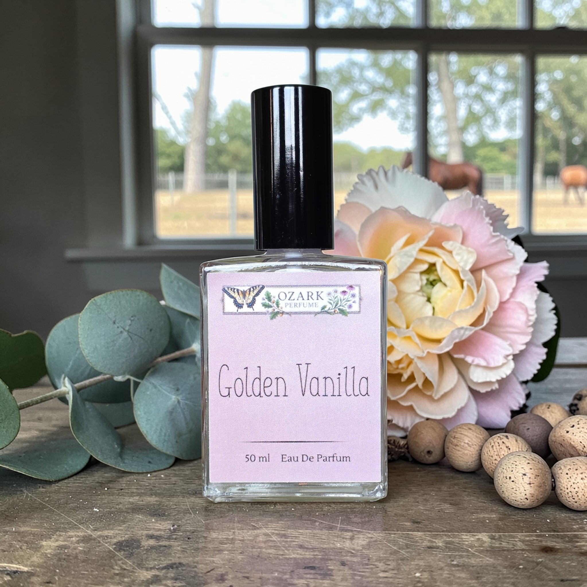 Perfume bottle labeled 'Golden Vanilla' with flowers and eucalyptus on a wooden surface.