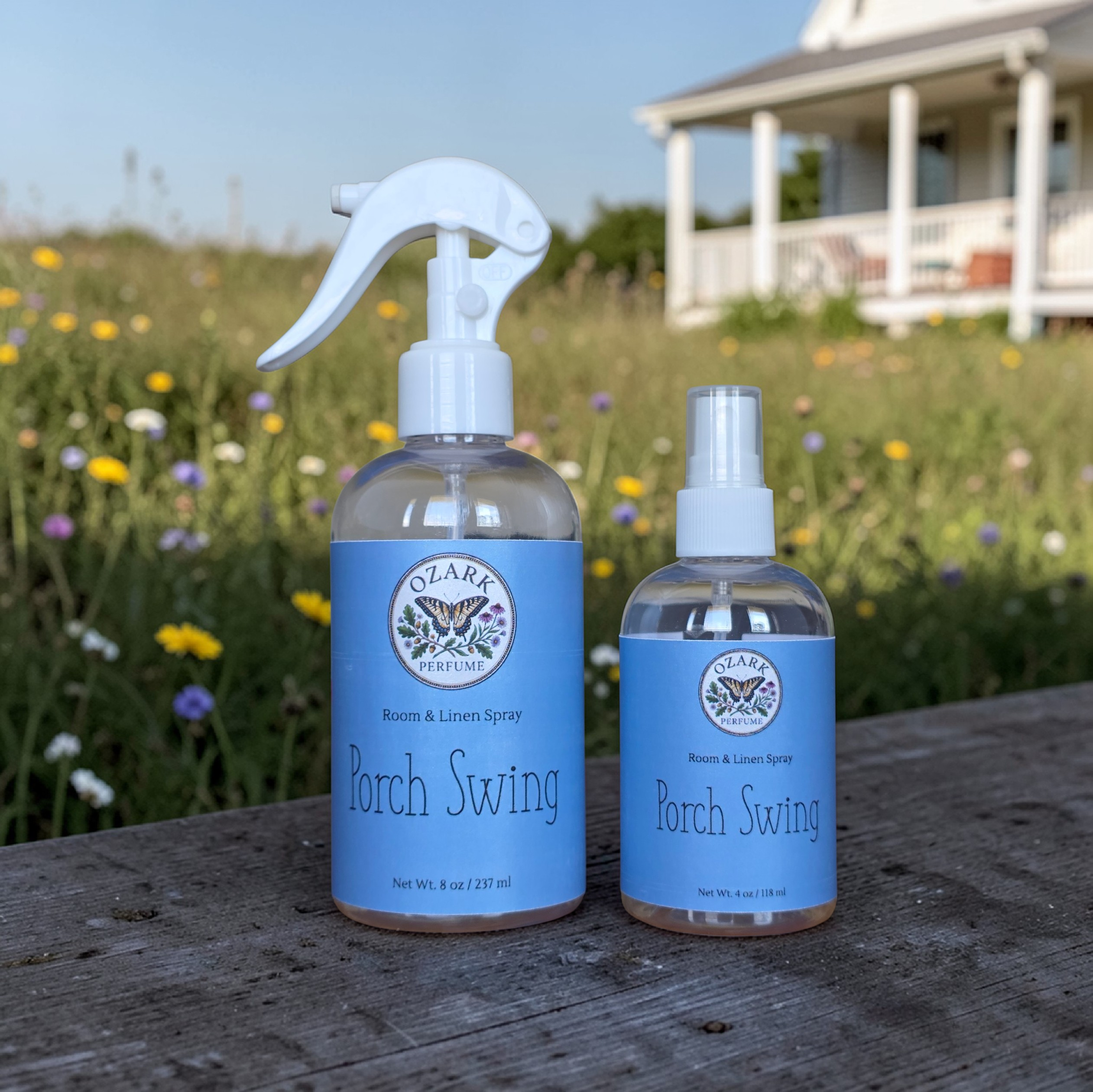 Two bottles of Ozarka Porch Swing room & linen spray on a wooden surface with a scenic background.