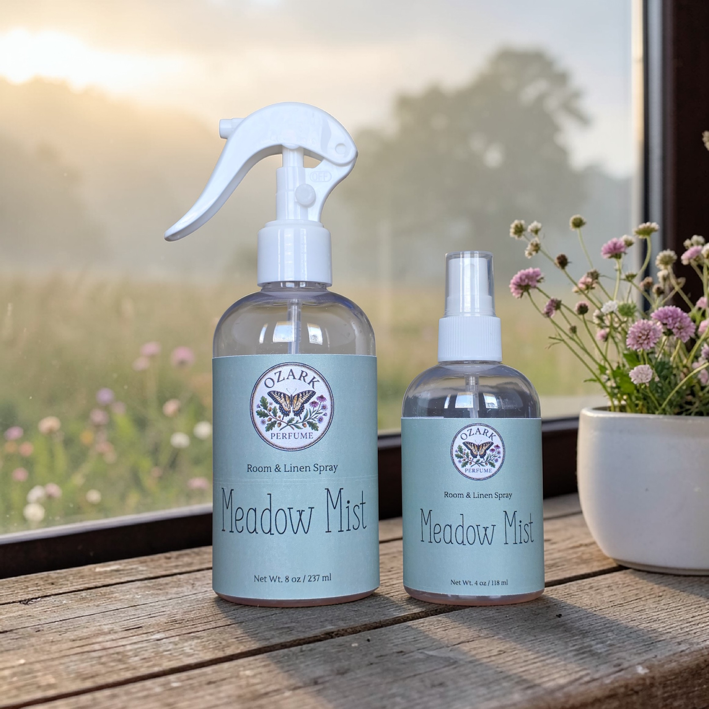 Two bottles of Ozara Meadow Mist room and linen spray on a wooden surface with a blurred natural background.