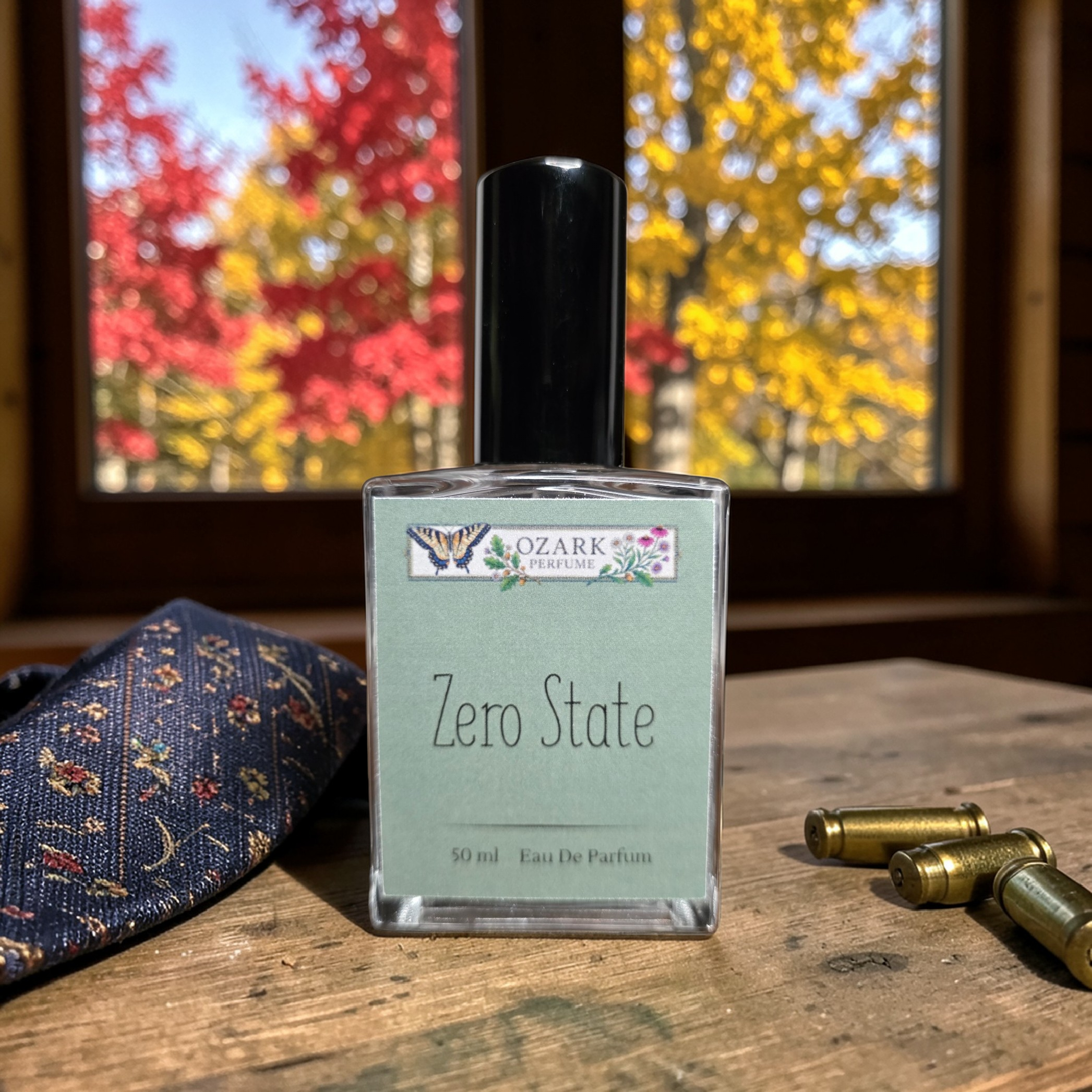 Perfume bottle labeled 'Zero State' by 'Ozark Perfume' on a wooden surface with autumn trees in the background.