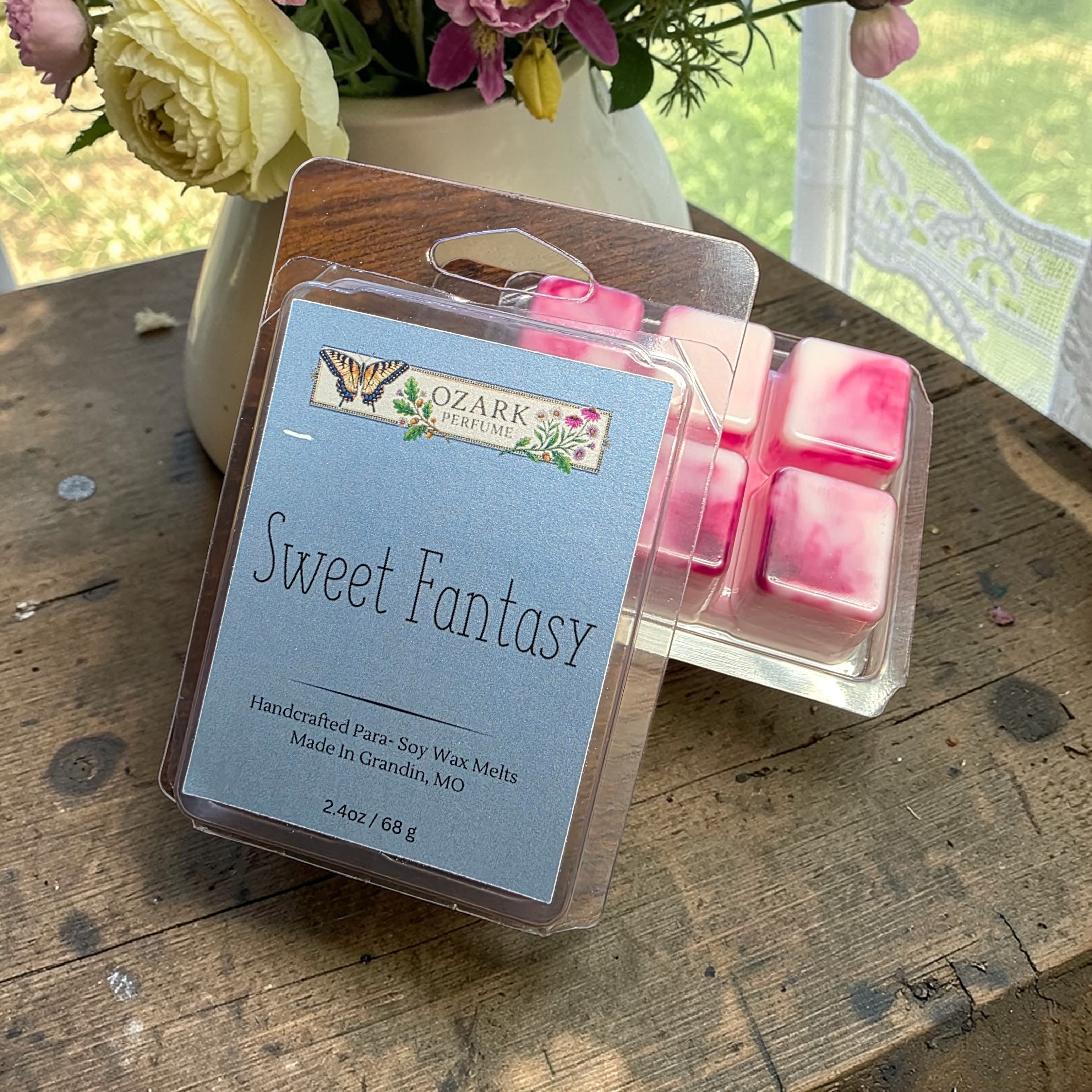 Ozark Perfume Art wax melts called sweet fantasy on a wooden surface with flowers in the background