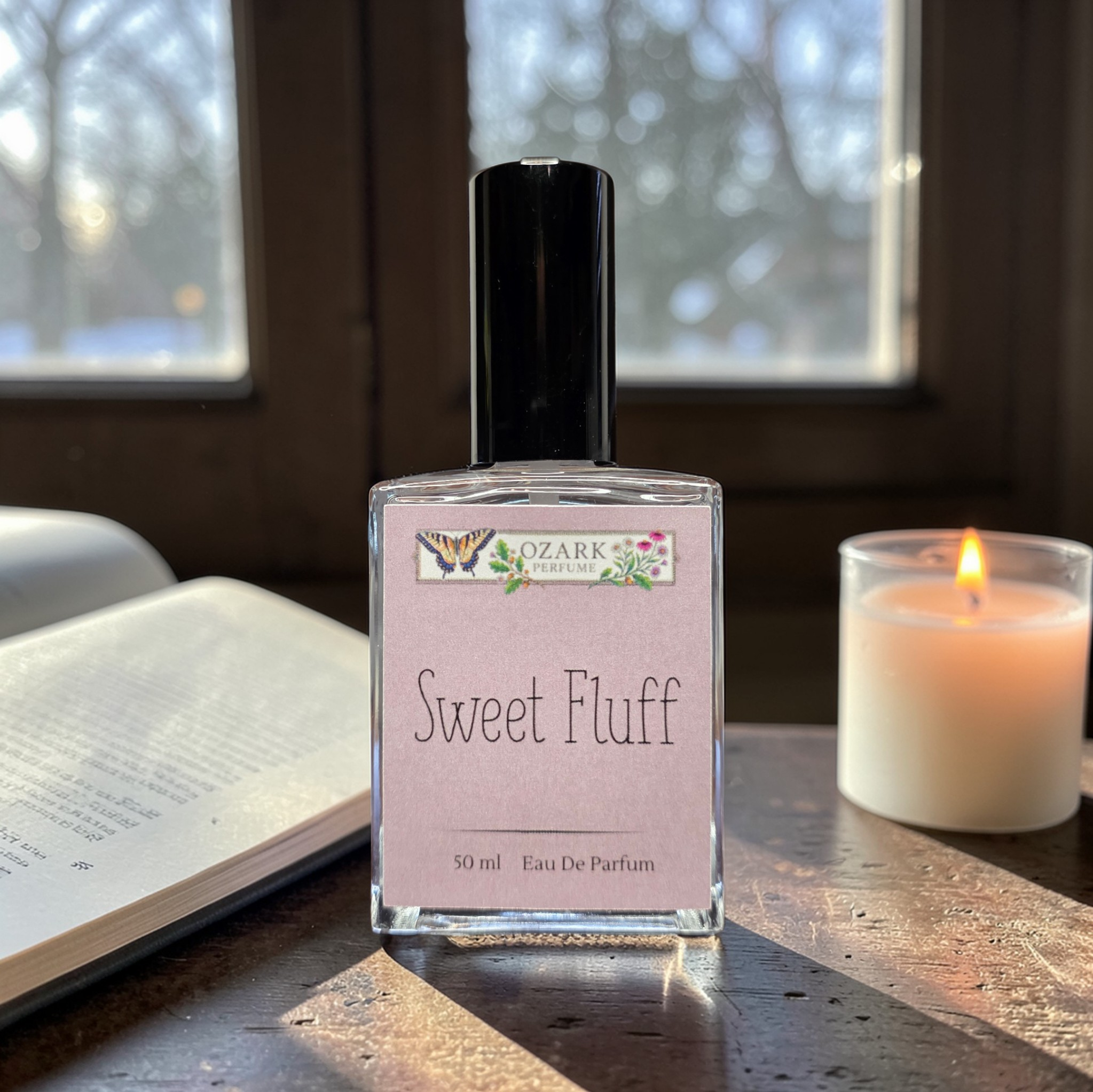 Bottle of 'Sweet Fluff' perfume by Ozark Aromatics on a wooden surface with a candle and book in the background.