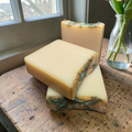 3 bars of soap stacked on a wooden surface with a vase of flowers in the background.