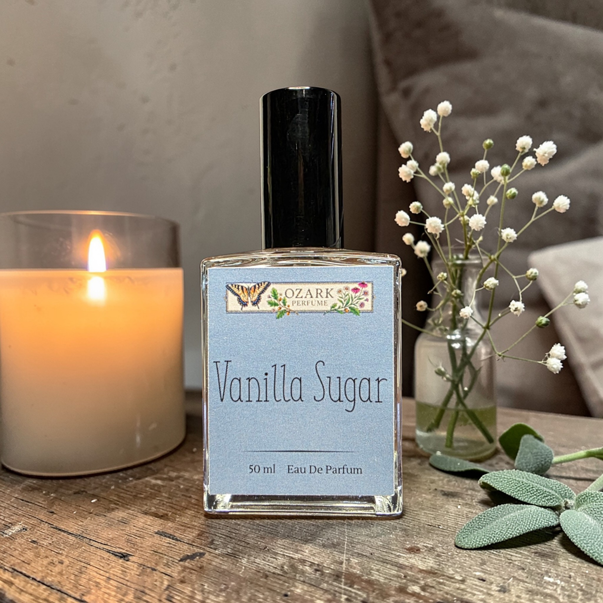 Vanilla Sugar perfume bottle on a wooden surface with a candle and flowers in the background